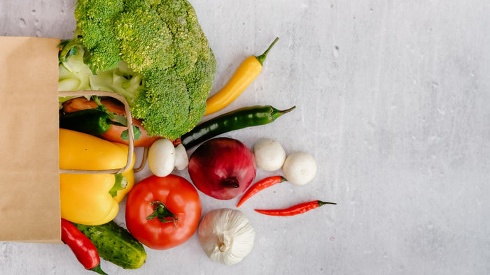 A brown paper bag with a variety of vegetables spilling out of it
