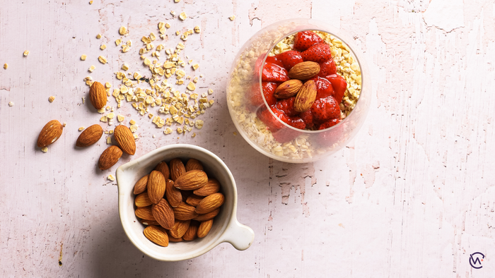 Roasted almonds in a jug next to a glass of porridge with strawberries on top