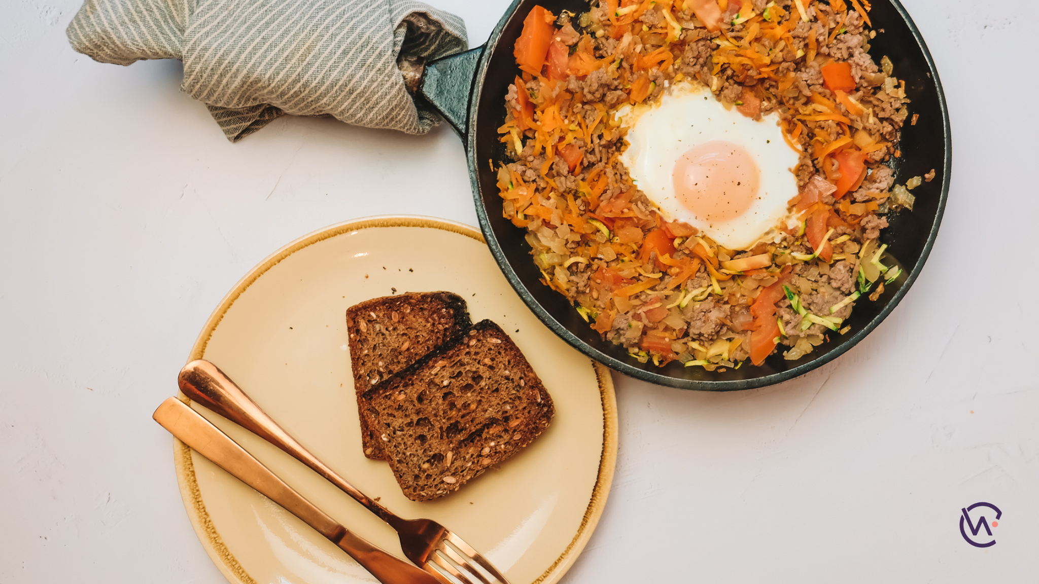 A pan with mince, vegetables and a fried egg, next to a plate with wholegrain bread