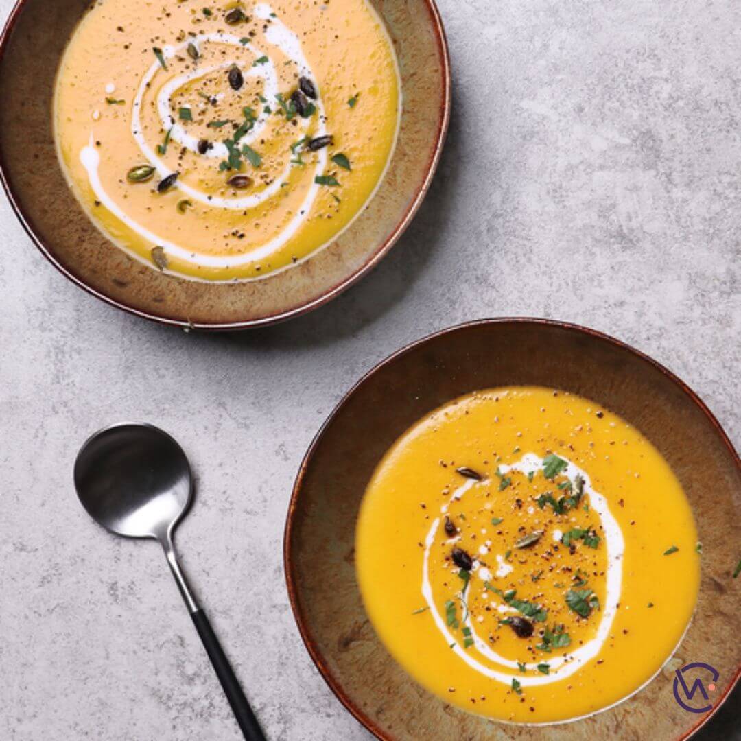 Two bowls of pumpkin Soup with cream drizzled on top with parsley