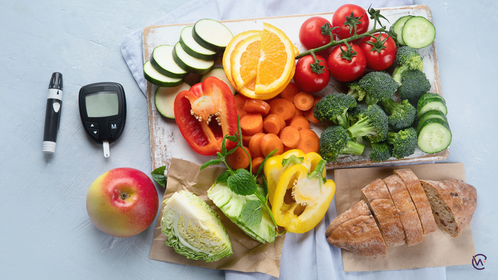 A variety of vegetables and fruit on a board with bread and a glucometer