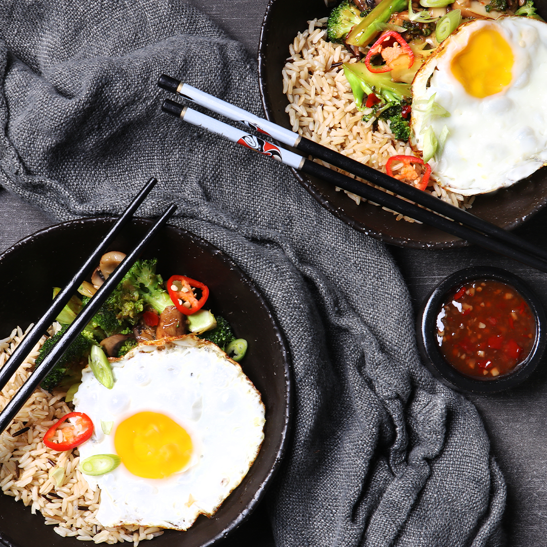 Two bowls with rice, sweet chilli vegetables, fried eggs and chopsticks 