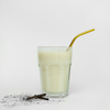 A prepared vanilla shake in a glass with a straw and vanilla pods next to it