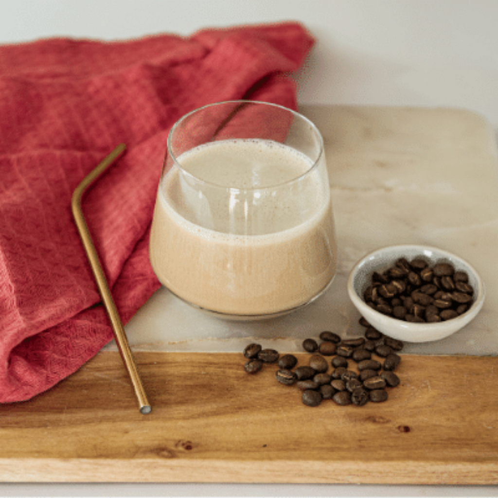 Prepare Cappuccino Shake in a glass with a straw, cloth and coffee beans next to it on a board