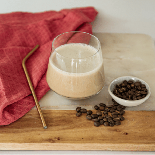 Prepare Cappuccino Shake in a glass with a straw, cloth and coffee beans next to it on a board