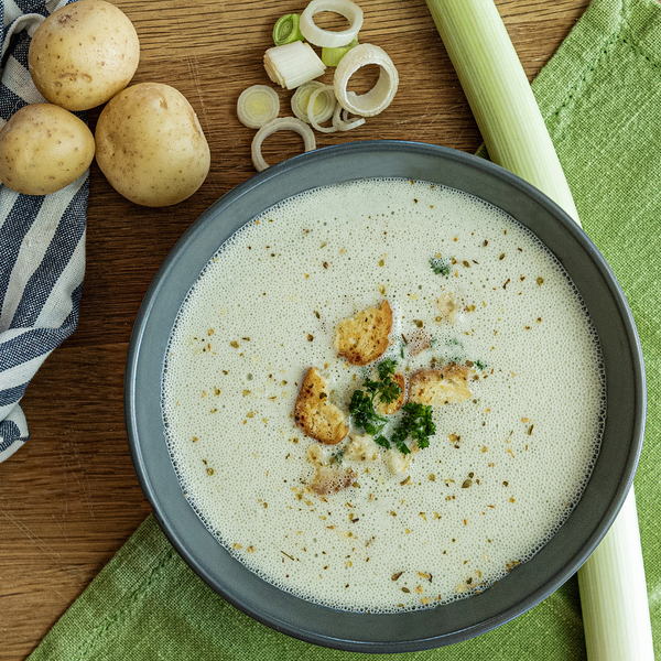 Prepared bowl of Potato and Leek Soup with potatoes, leeks and napkin next to it